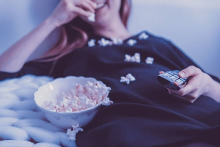 Girl eating popcorn and smiling with remote control in hand.