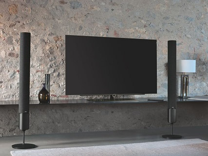 Flat screen tv against stone wall with surround sound speakers.
